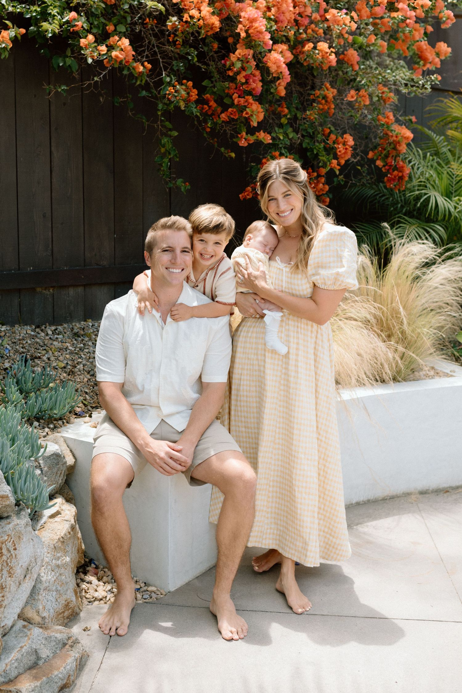 A smiling family of four poses outdoors with vibrant orange bougainvillea blooms behind them.