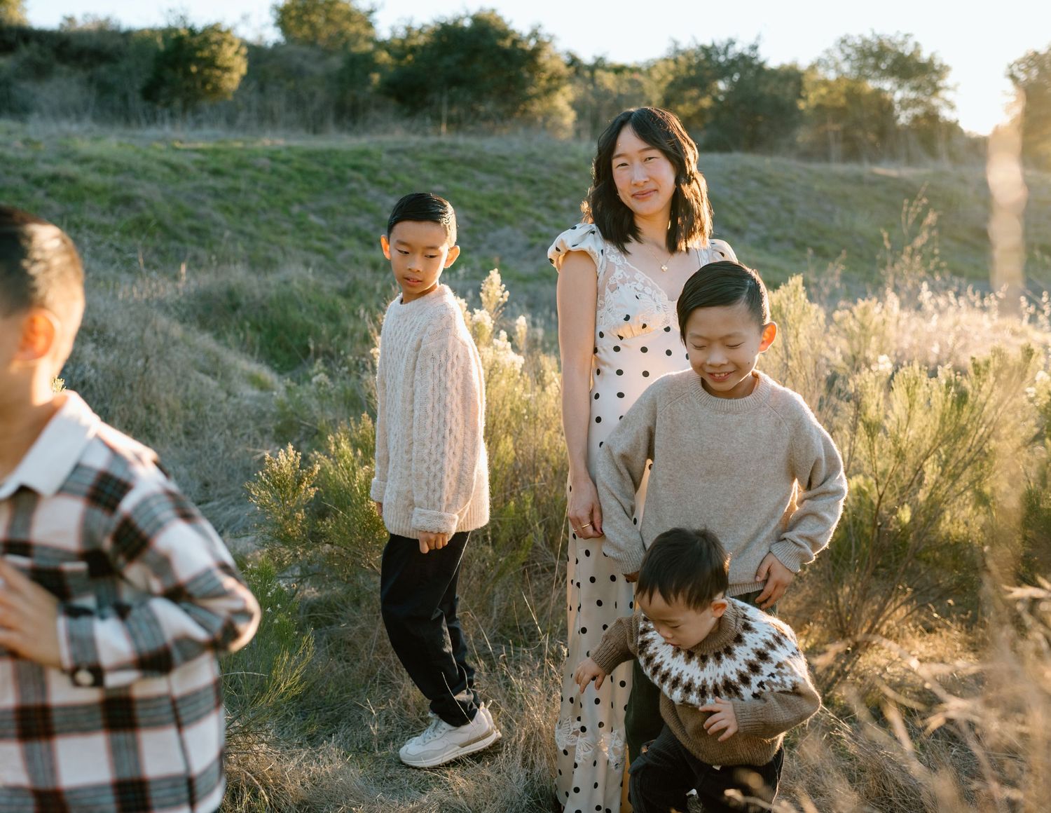 An Asian mother stands with her three sons in a golden sunlit field during a family portrait session.
