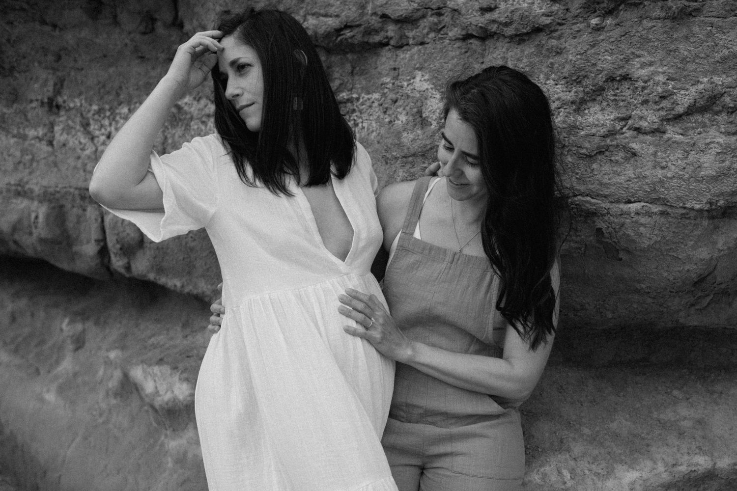 Two women posing together against a stone wall in black and white outdoor portrait photo.