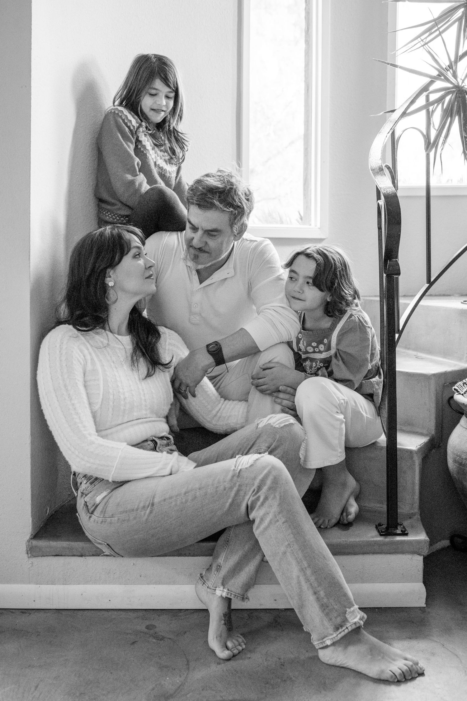 Black and white photo of a happy family of four sitting together on indoor steps.