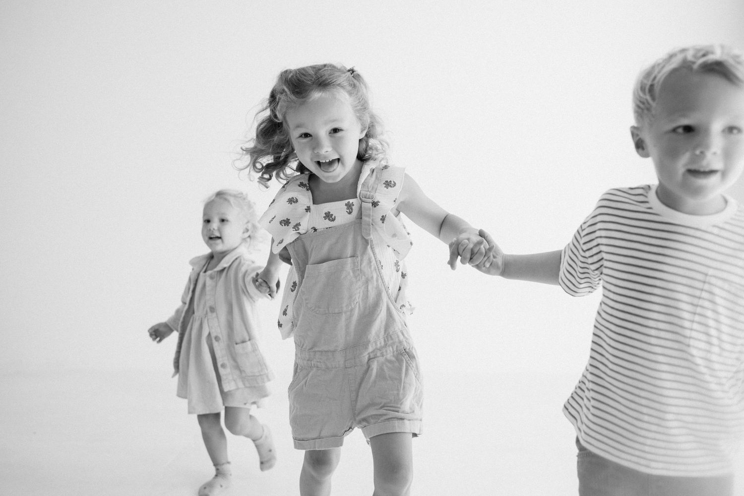 Black and white photo of three young children running and holding hands joyfully.