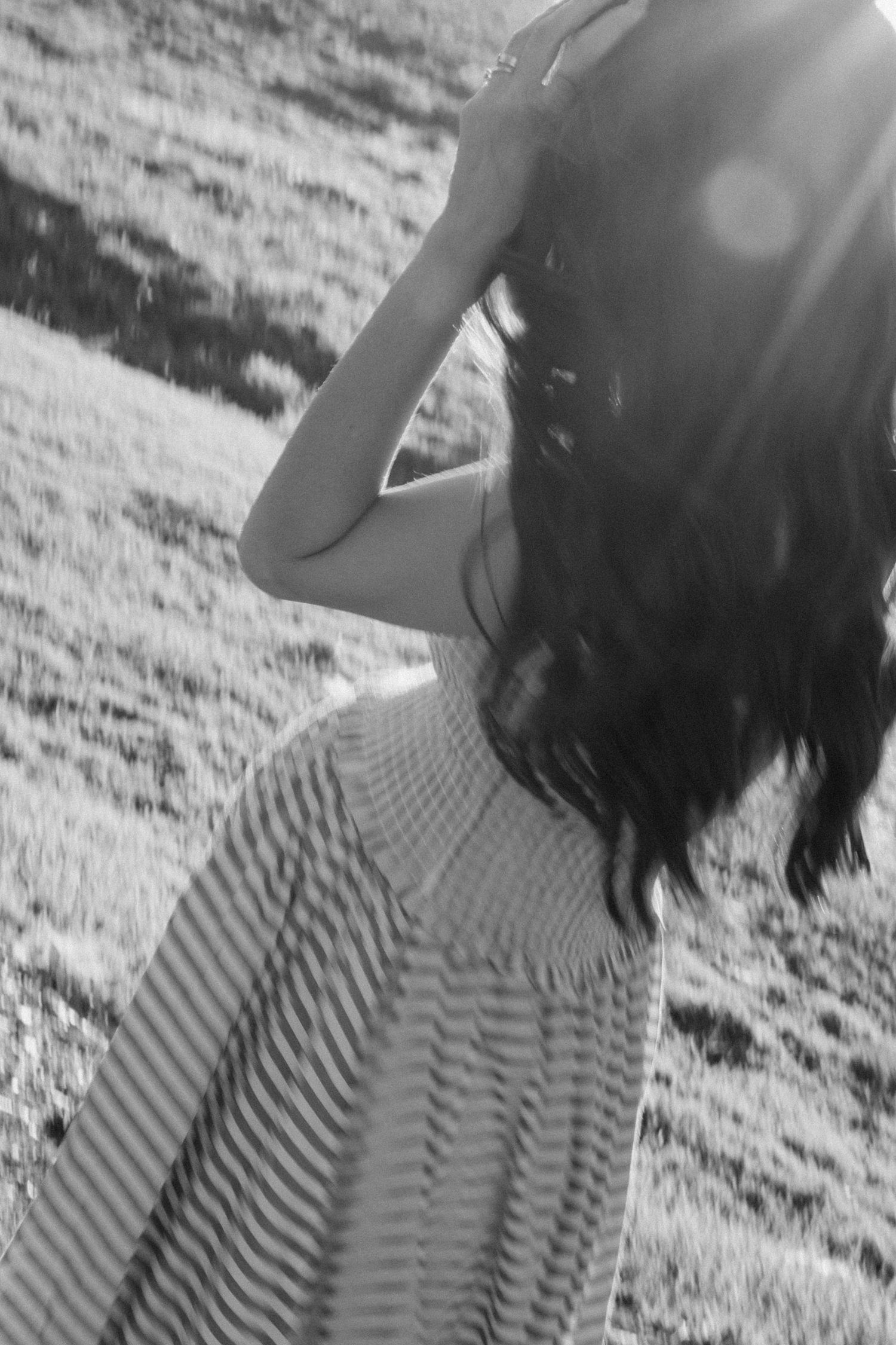 Black and white back view of pregnant woman in striped dress in sunlight.