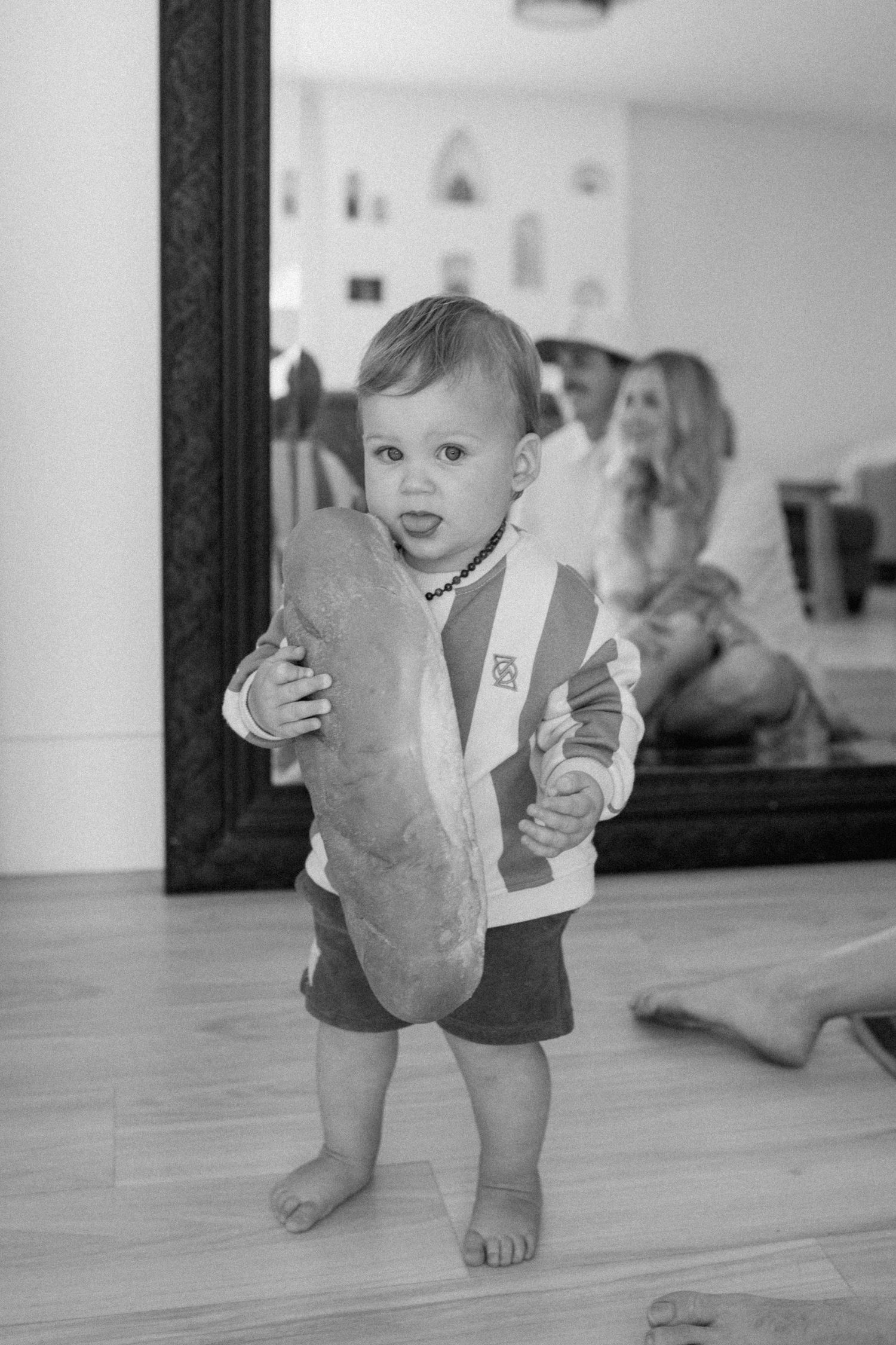 Three black and white photographs show a cheerful baby wearing a vest and shorts crawling on a hardwood floor.
