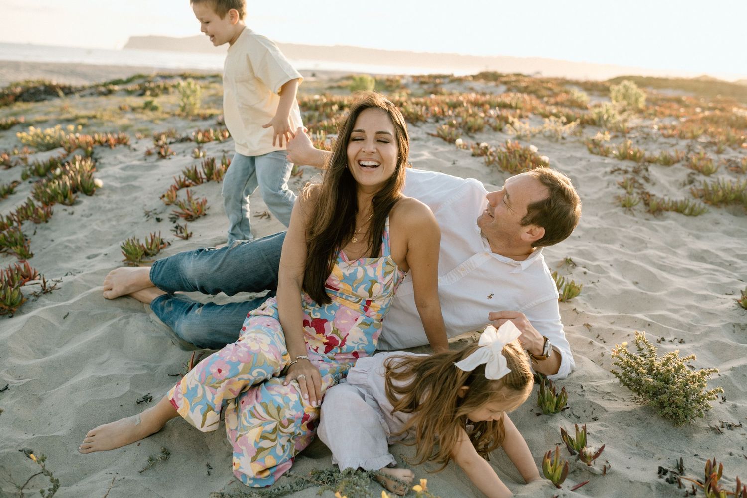 A happy family relaxes together on sandy beach dunes at golden hour sunset.
