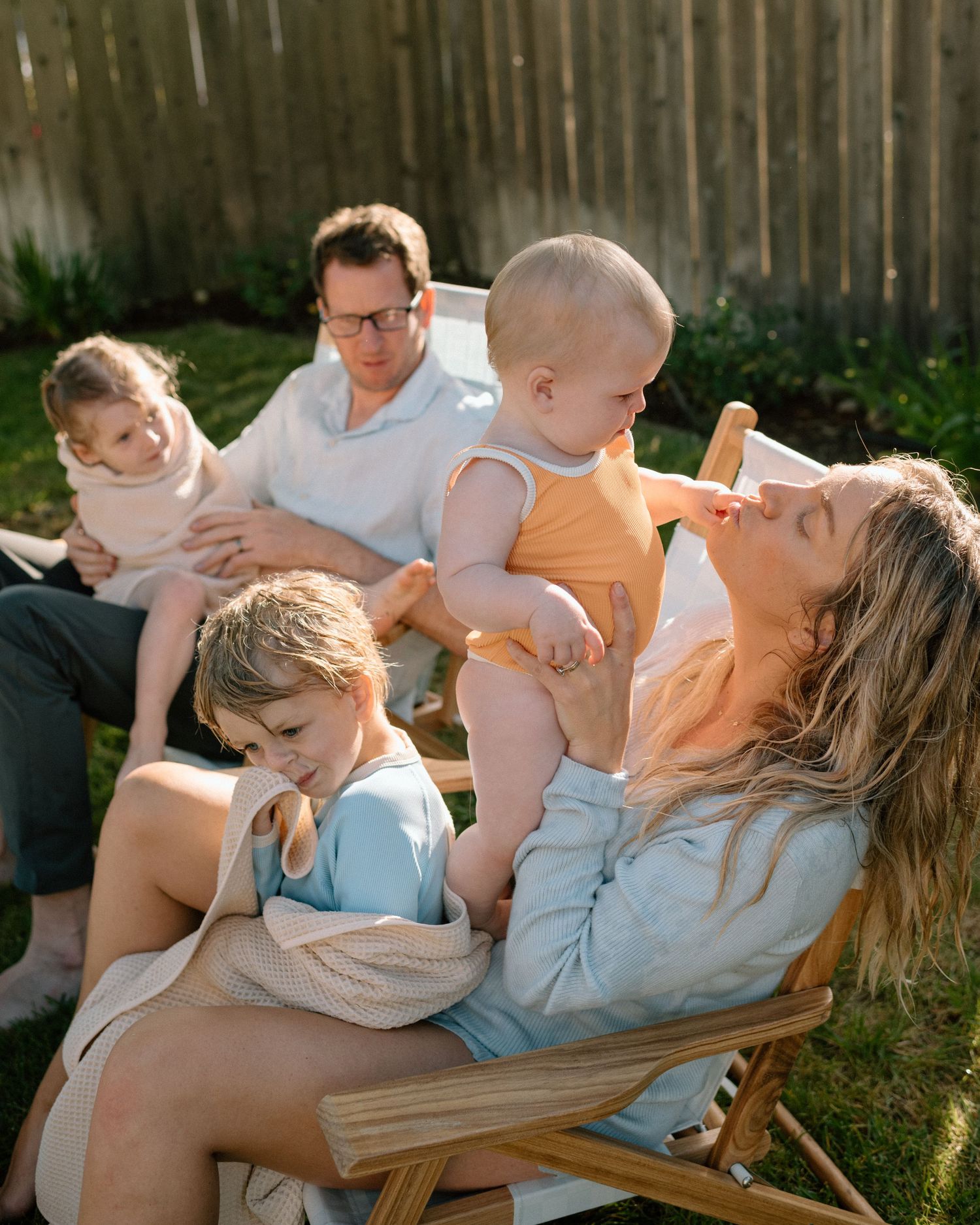 Family of five relaxing together in garden chairs in warm golden afternoon light.