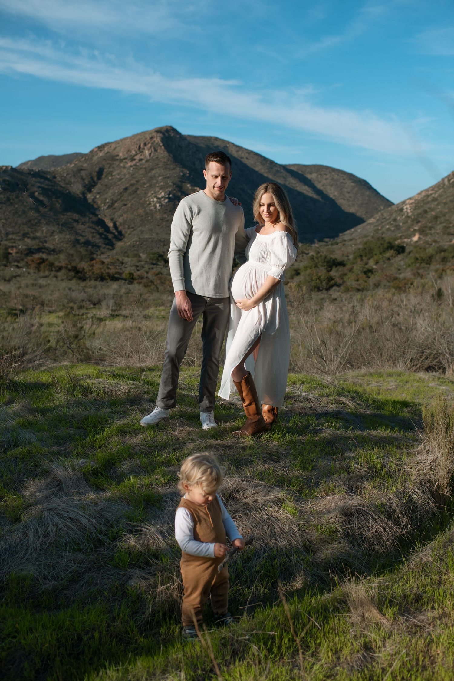 Family maternity photo with couple and toddler standing in a green mountain meadow.