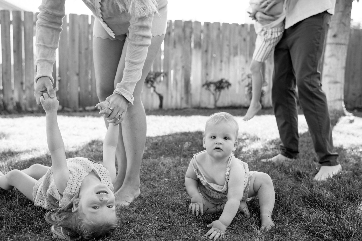 Black and white photo of parents playing with two babies on a sunny lawn.