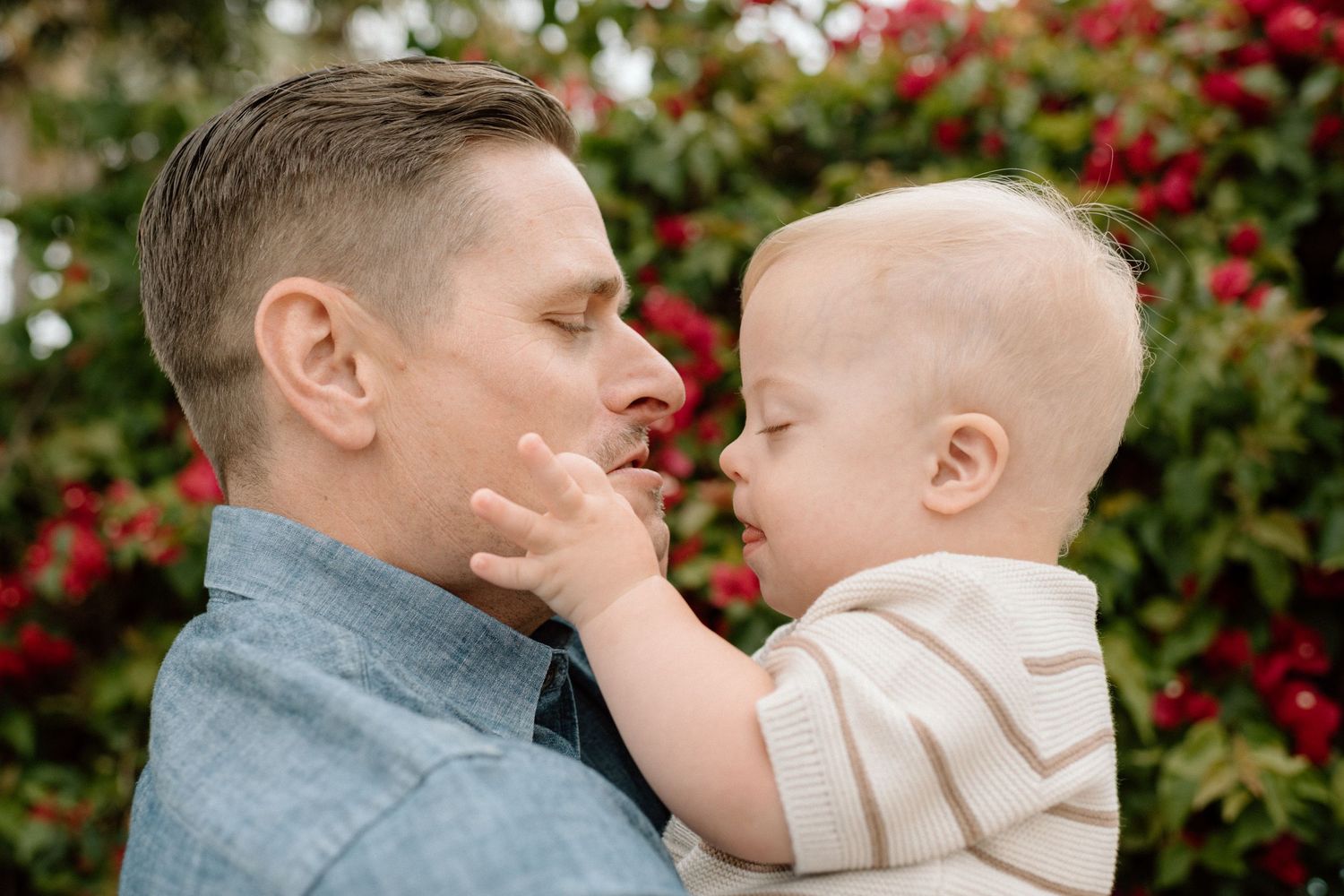 Loving father holding toddler son close, sharing a tender nose-to-nose moment outdoors.