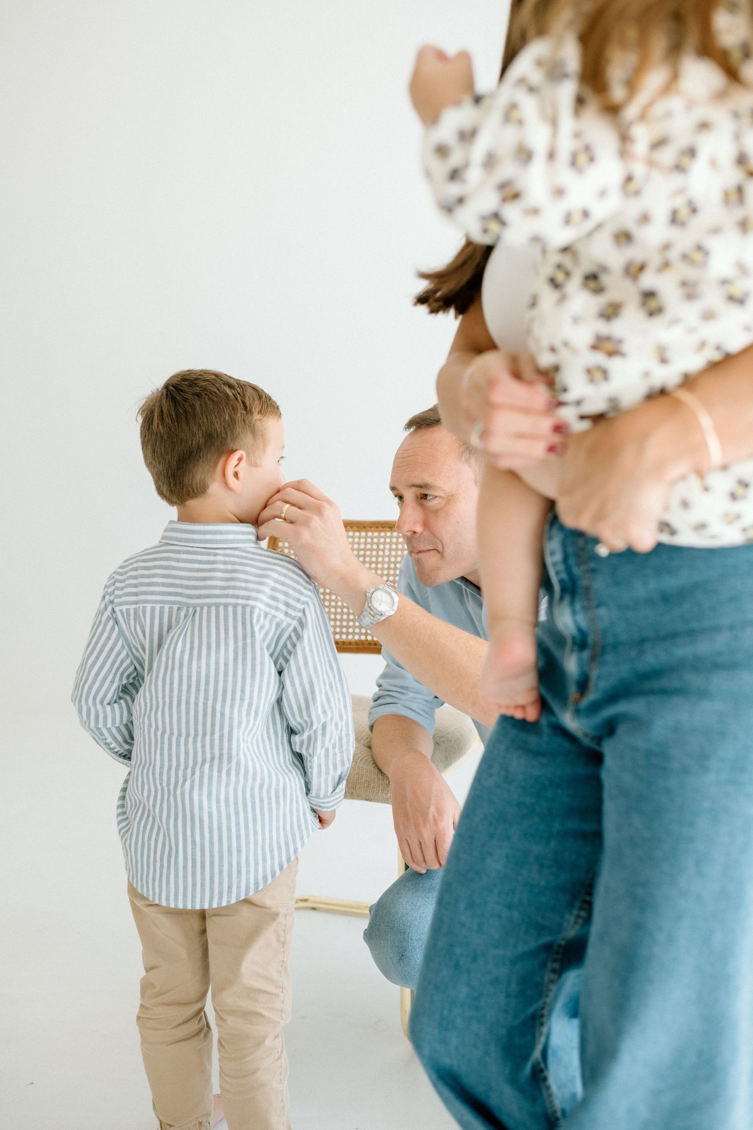Father kneeling to talk with young son in striped shirt in white studio.