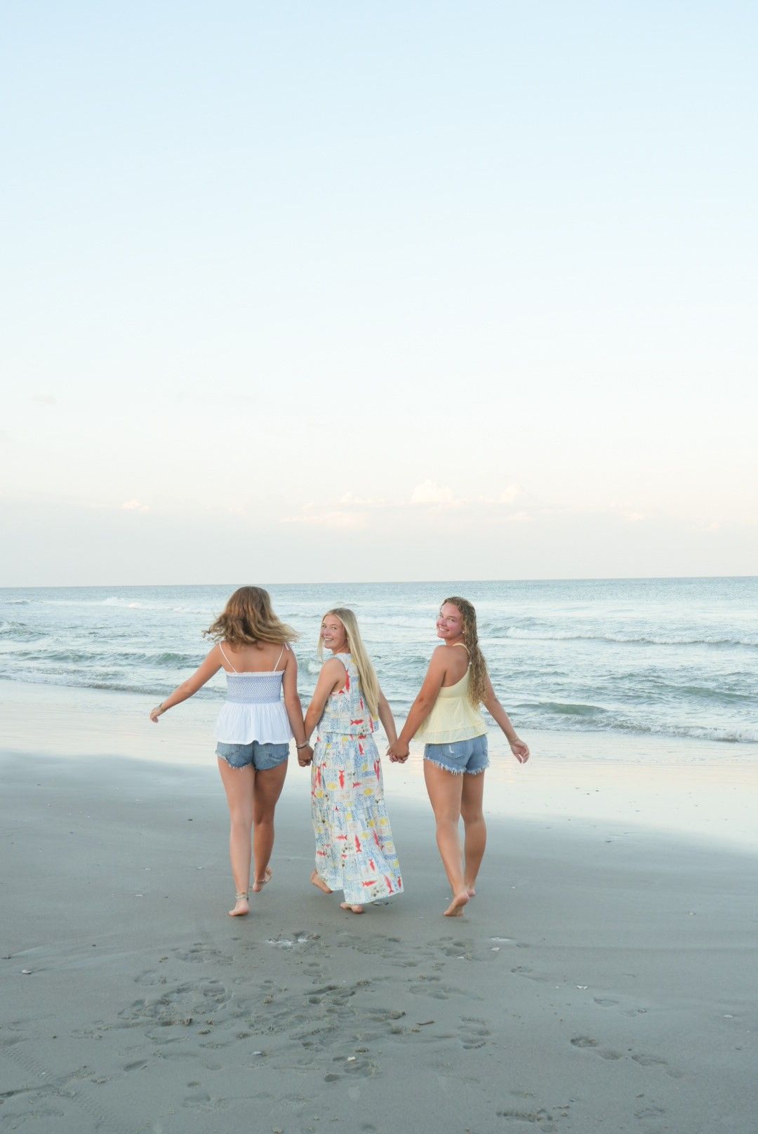Three sisters walking down the beach during a family photoshoot in Pawleys Island, South Carolina.