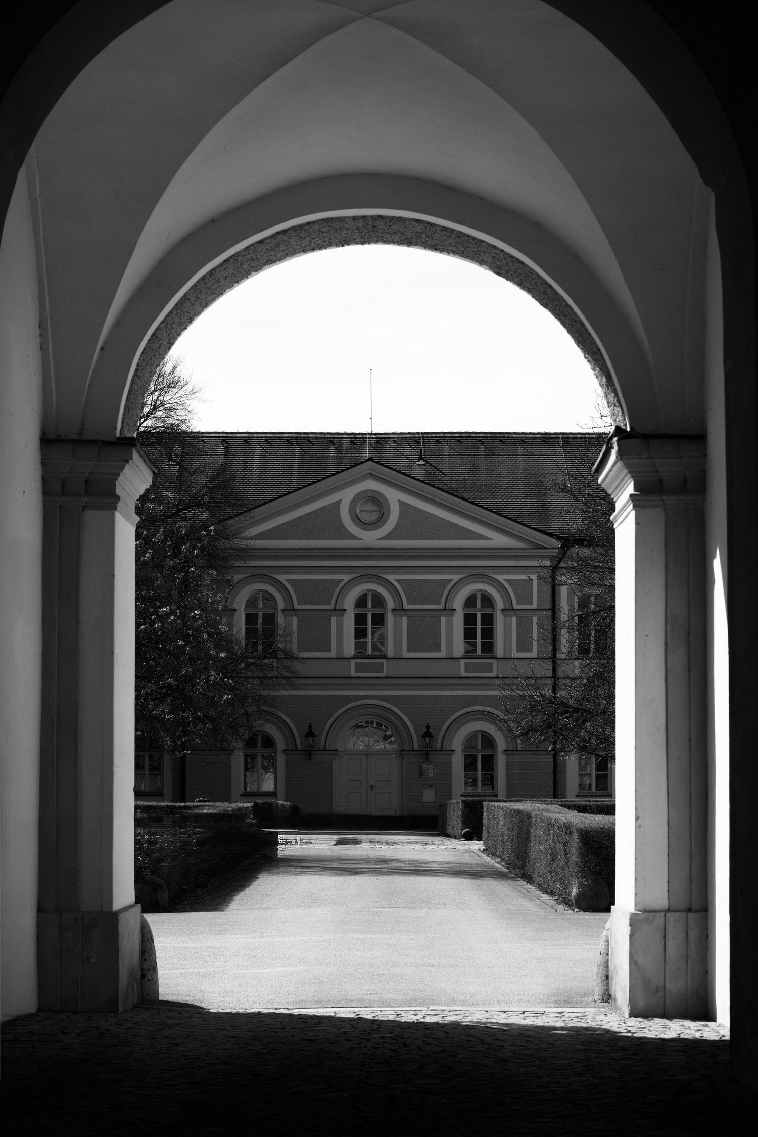 Black and white photo of a classical European building viewed through an arched stone gateway.