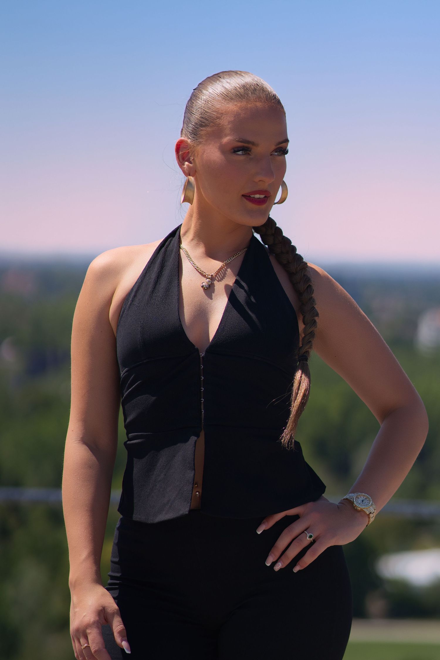 Blonde woman in black halter top with braided hair posing outdoors on sunny day.