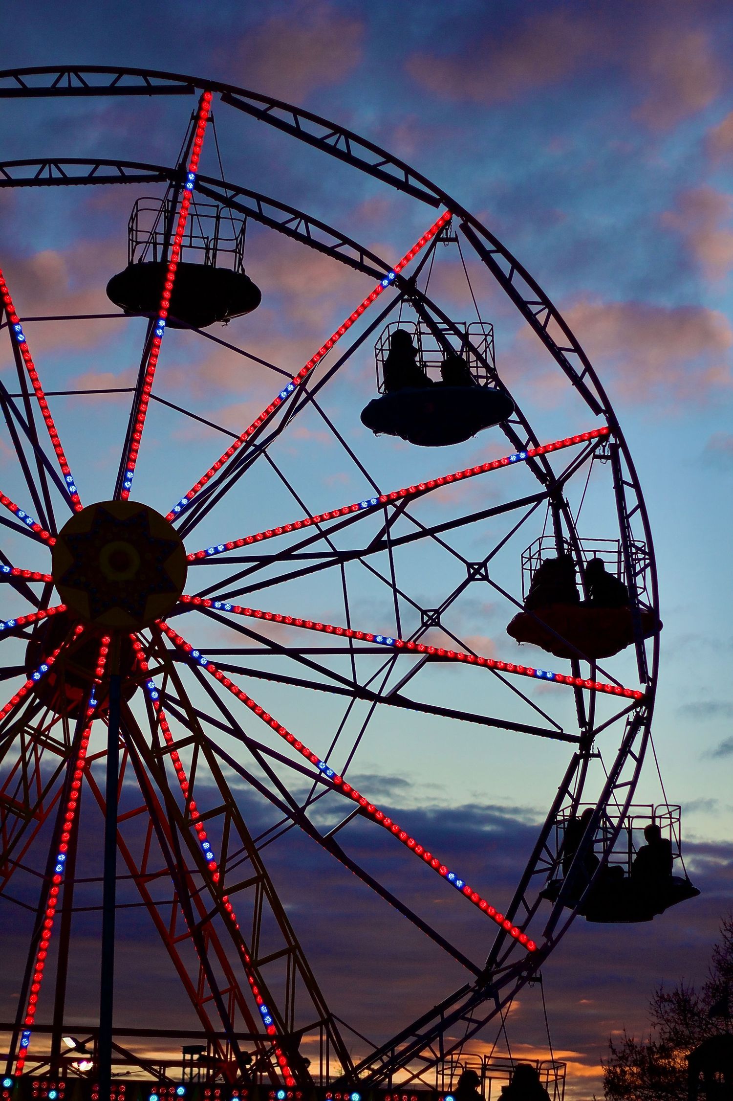 Colorful Ferris wheel with red and blue lights silhouetted against a vibrant sunset sky at a fair.
