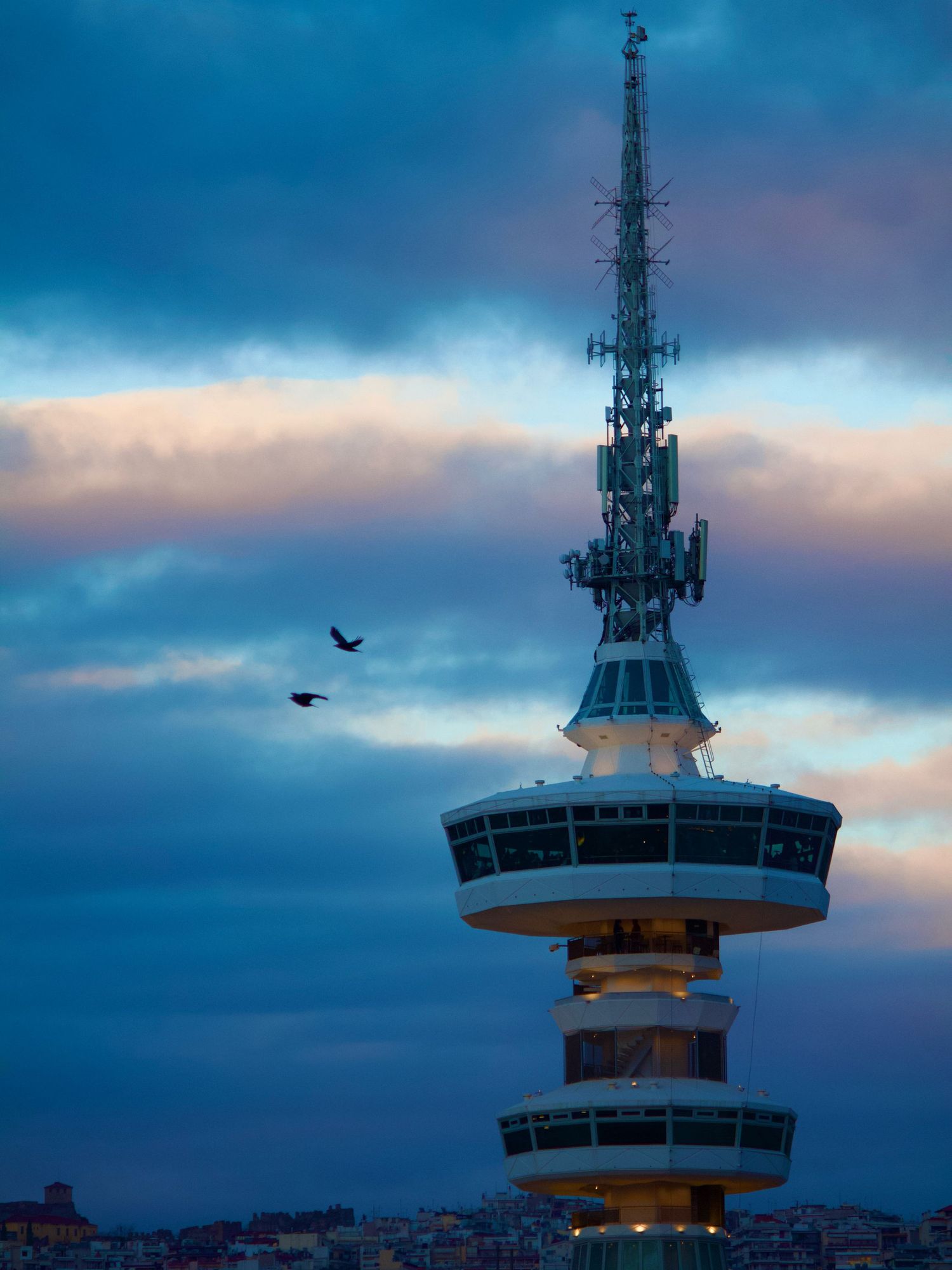 OTE telecommunications tower against a dramatic blue cloudy sky at dusk with birds flying past.