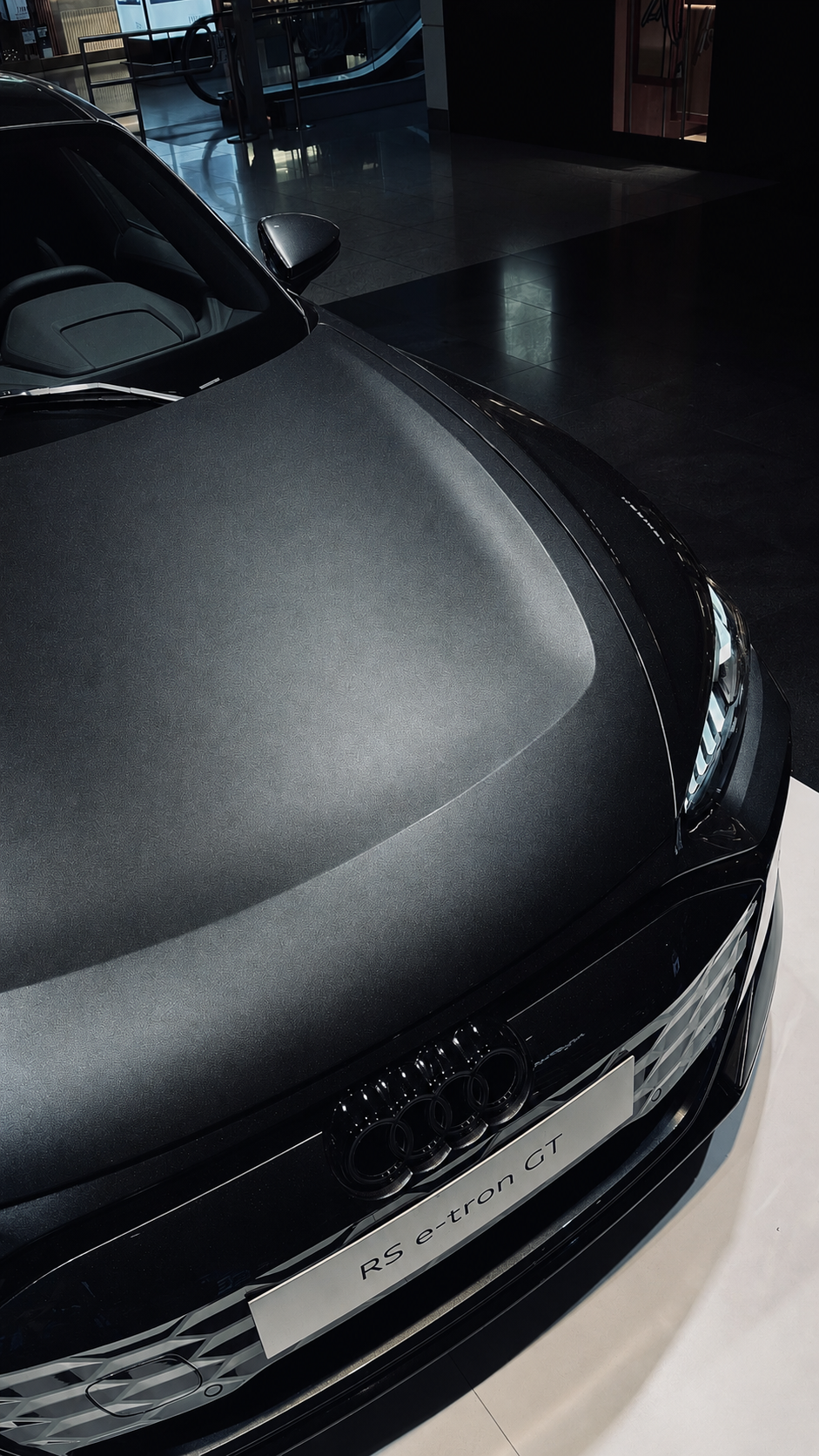 Close-up of matte black Audi RS e-tron GT hood in luxury showroom.