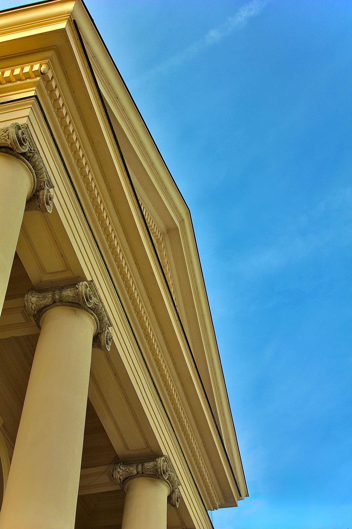 Low angle view of classical building with Ionic columns and ornate cornice against a bright blue sky.