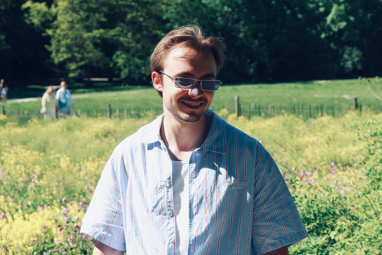 Smiling man wearing sunglasses standing in a sunny green meadow on a bright summer day.