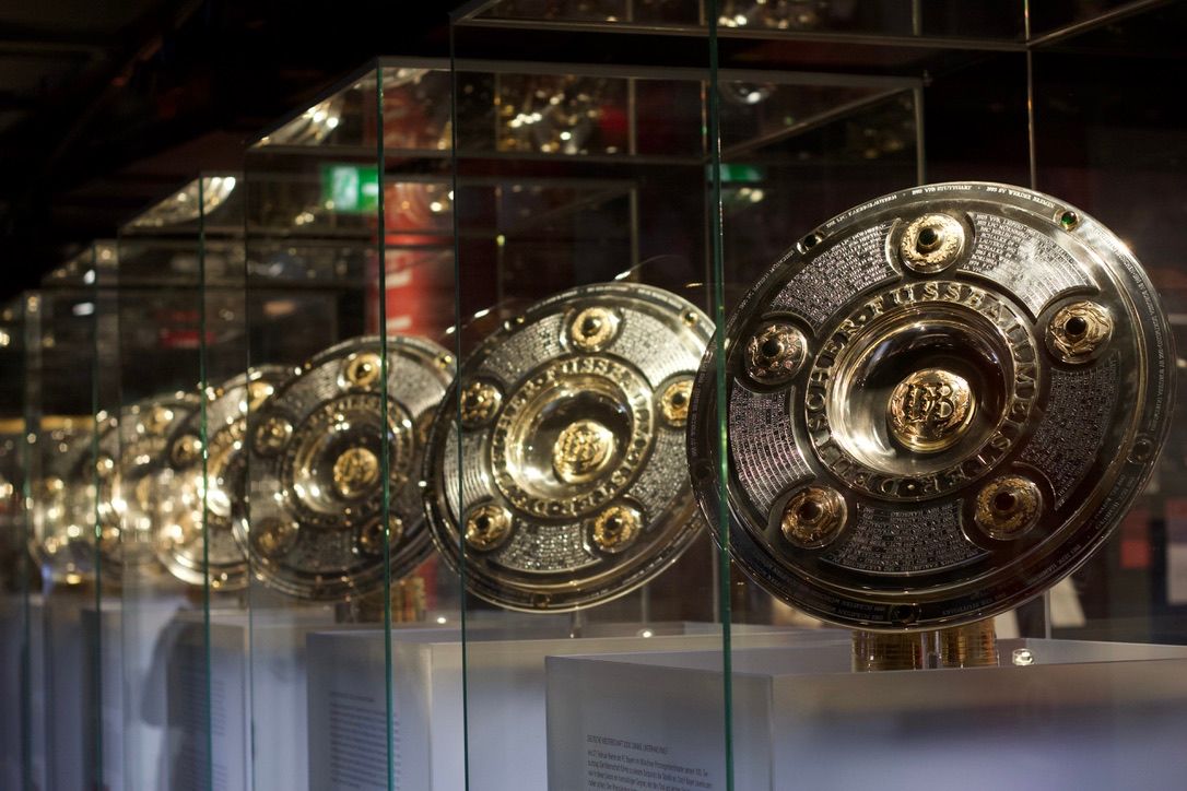 Row of Bundesliga Meisterschale championship trophies displayed in glass cases at museum.