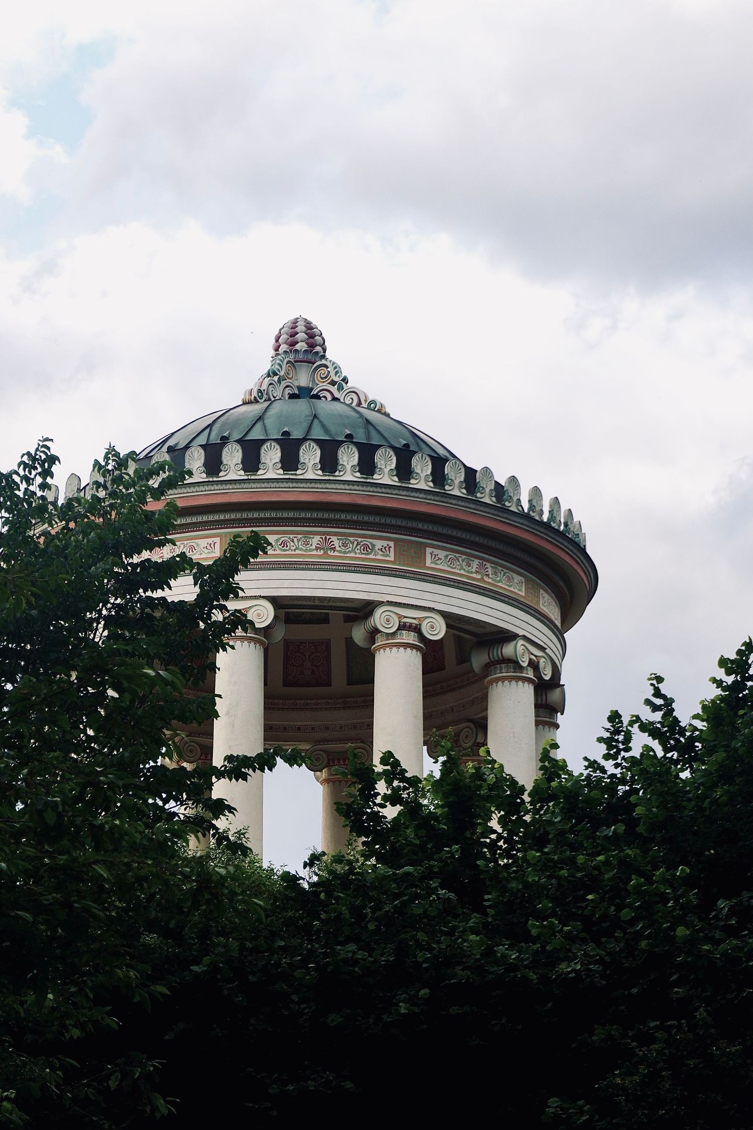 Ornate neoclassical rotunda pavilion with columns and decorative dome surrounded by trees.