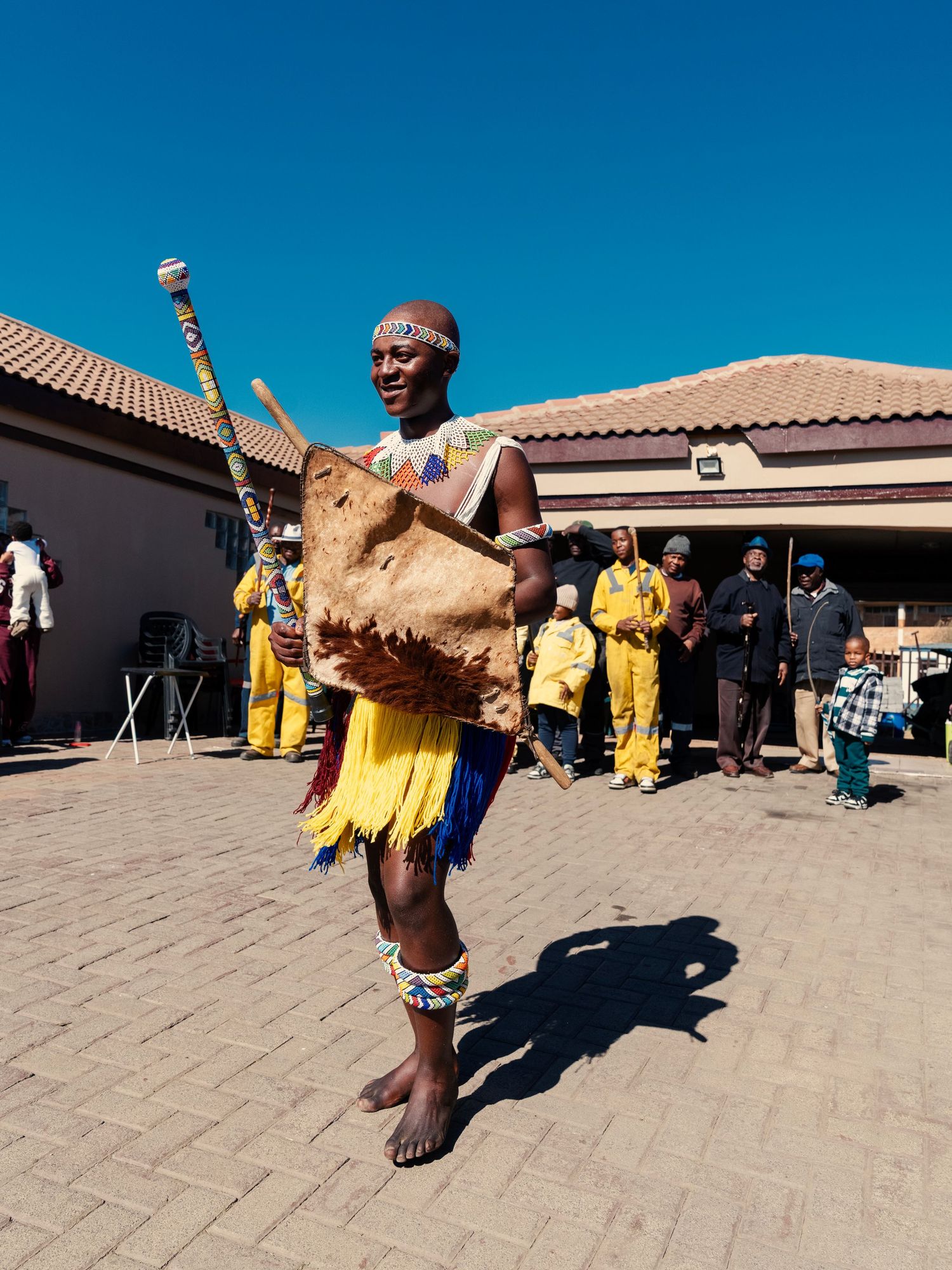 Traditional African dancer in yellow beaded costume performs with drum at cultural ceremony outdoors. Event Photography