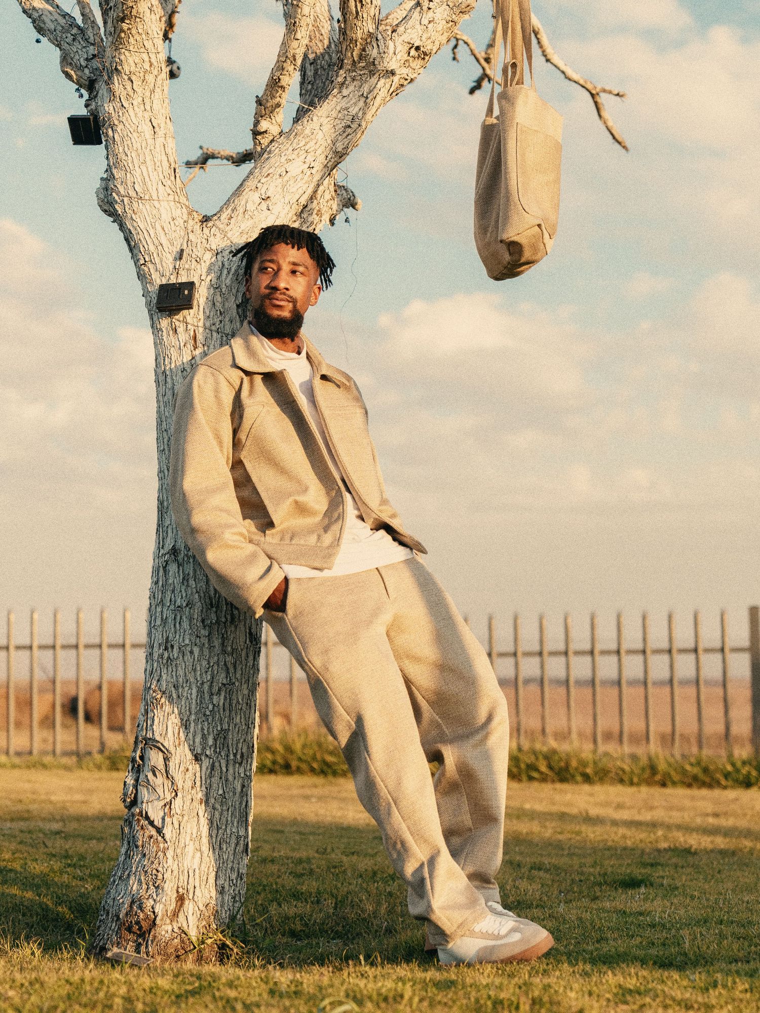 Fashionable man in tan linen suit leaning against bare tree outdoors. Fashion Photography