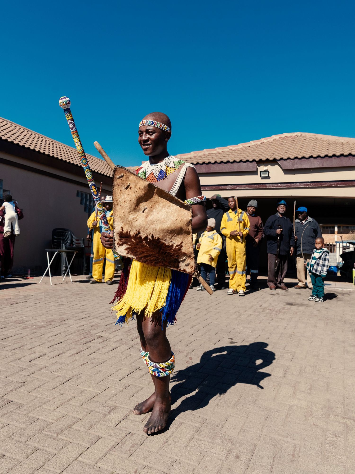 Zulu dancer in traditional yellow fringe skirt and beaded accessories carrying a drum during cultural celebration. Event Photography