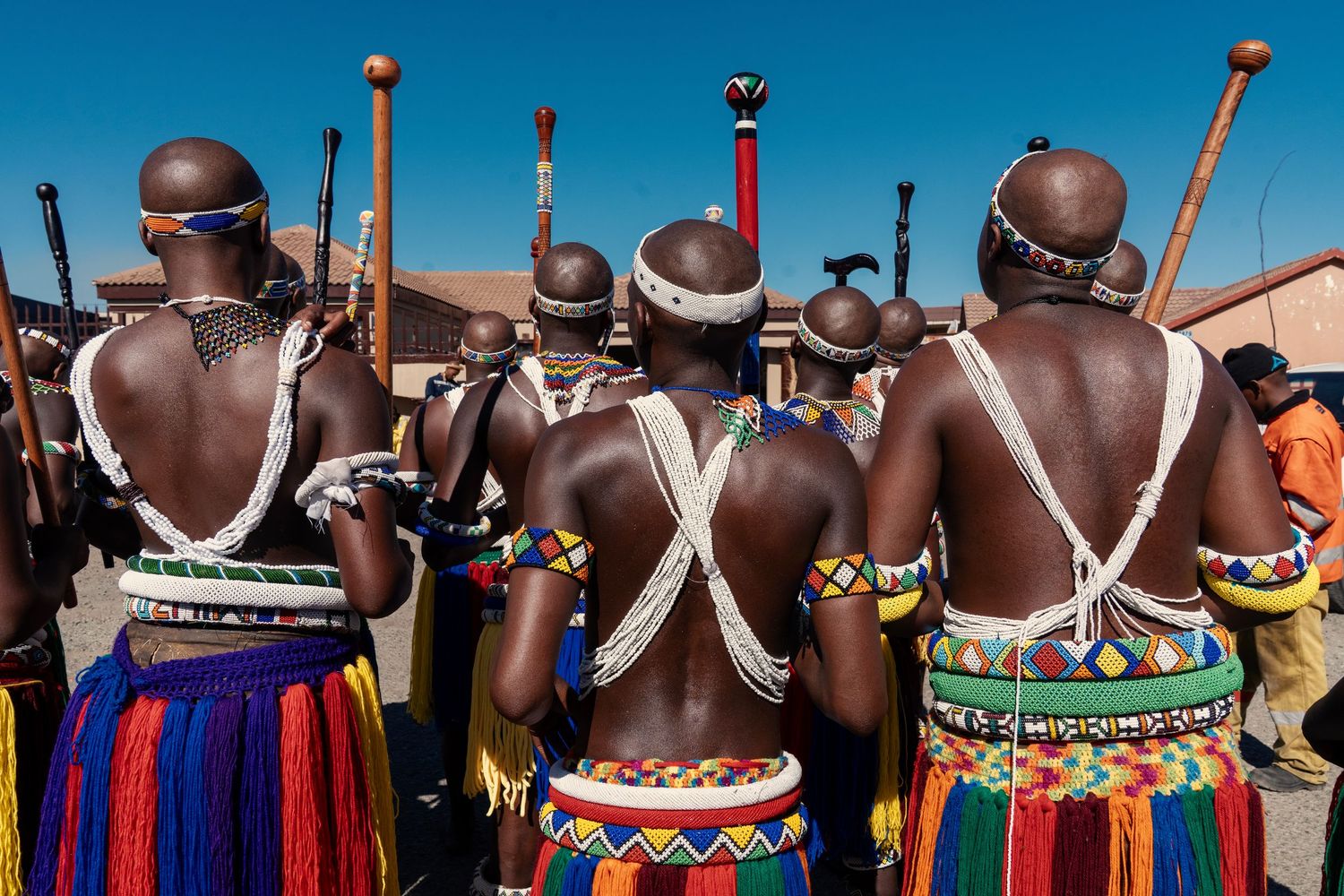 Back view of Zulu dancers in traditional colorful beaded costumes and fringe skirts during a cultural ceremony. Event Photography
