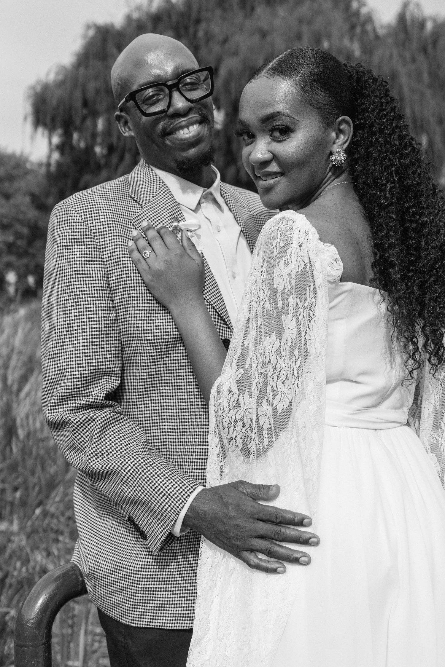 Black and white wedding portrait of a joyful couple embracing, groom in plaid suit and bride in white lace dress.