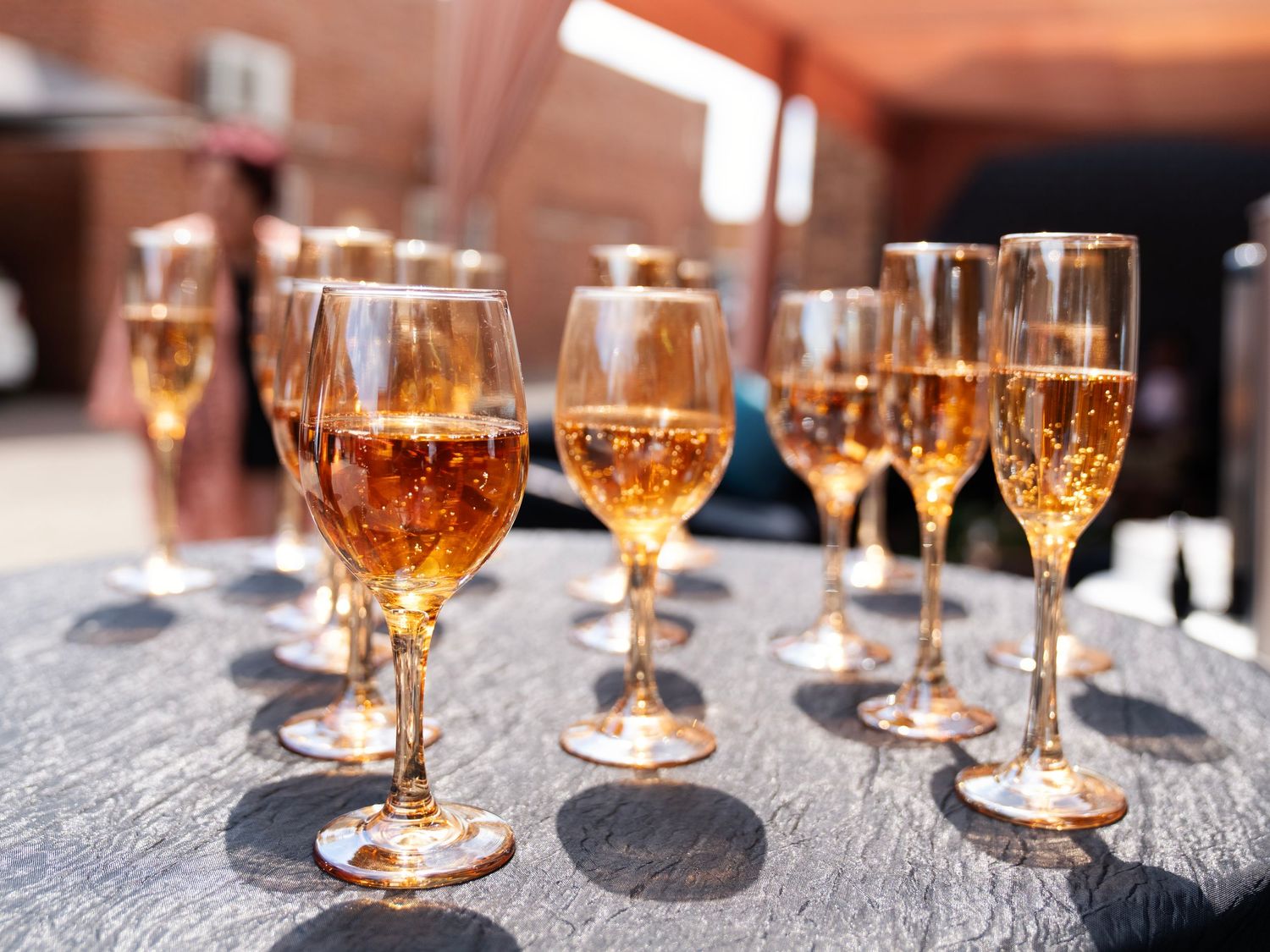 Rows of sparkling rose champagne flutes arranged on a table in bright sunlight at a wedding reception.