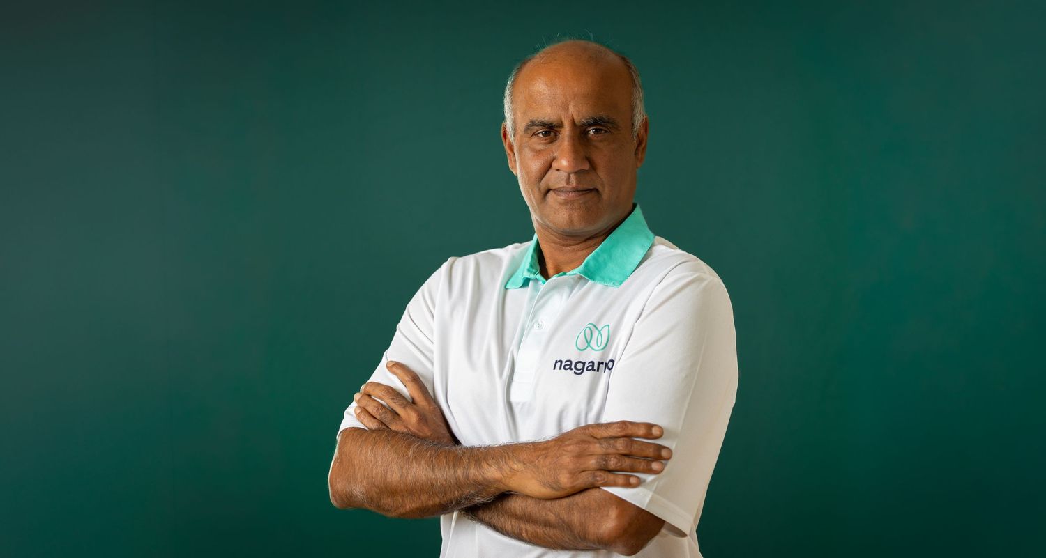 A person in a white polo shirt stands with arms crossed against a dark green background.
