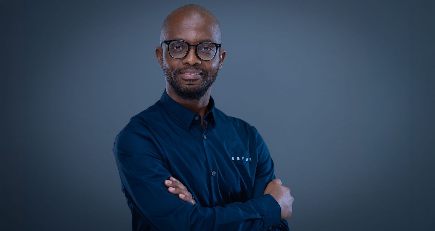 Professional man in dark blue shirt with arms crossed, smiling confidently against a gray studio background.