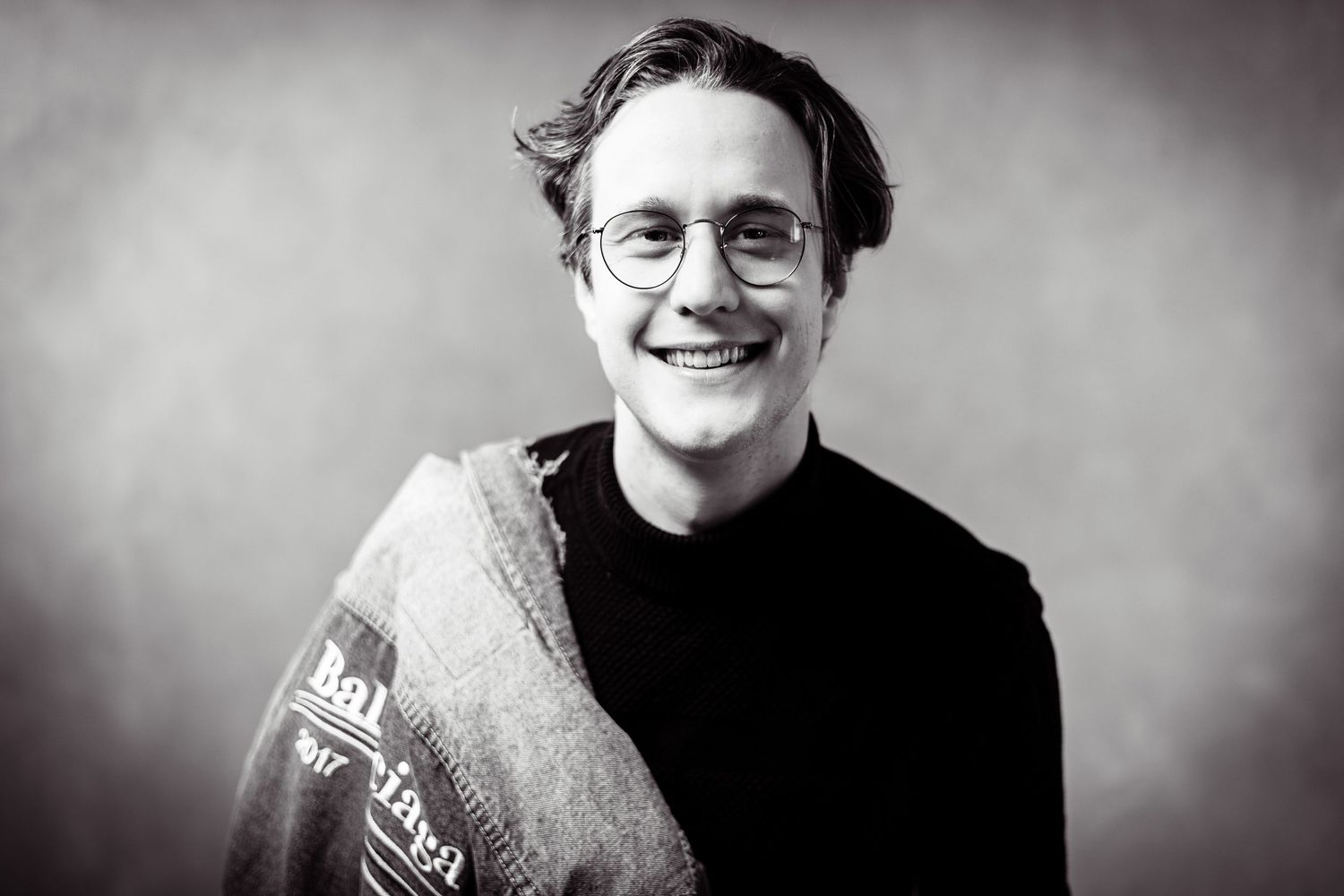 Black and white portrait of someone in glasses wearing a casual sweater and smiling at the camera.