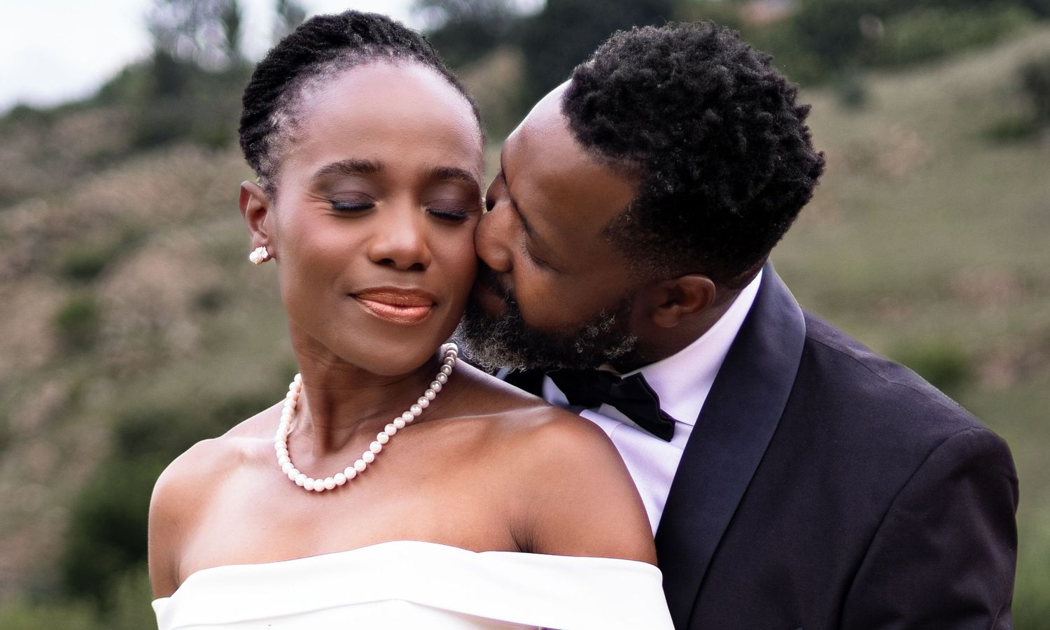 A couple shares intimate moments in formal wedding attire against a scenic outdoor backdrop.