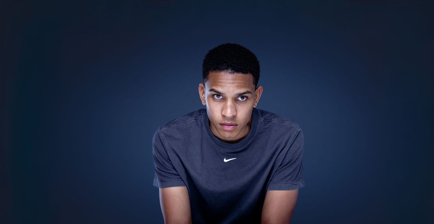 Athletic man in a grey Nike t-shirt poses against dark blue backdrop in dramatic lighting.
