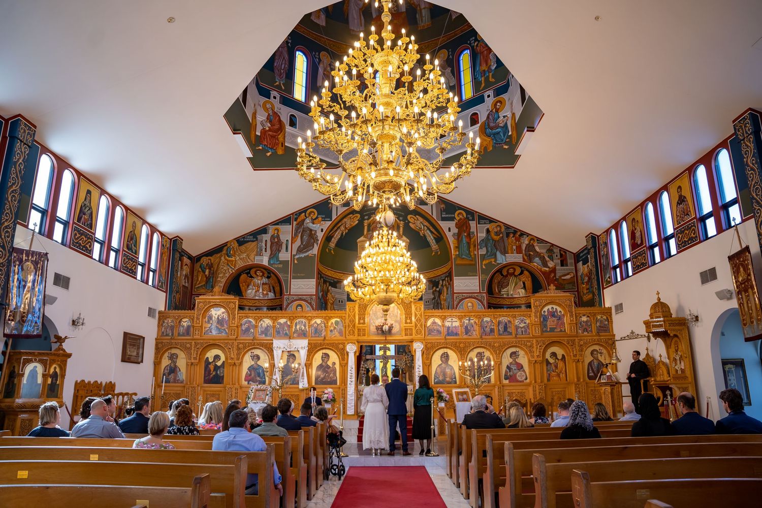 Ornate Orthodox church interior with golden chandelier and iconostasis during a wedding ceremony.