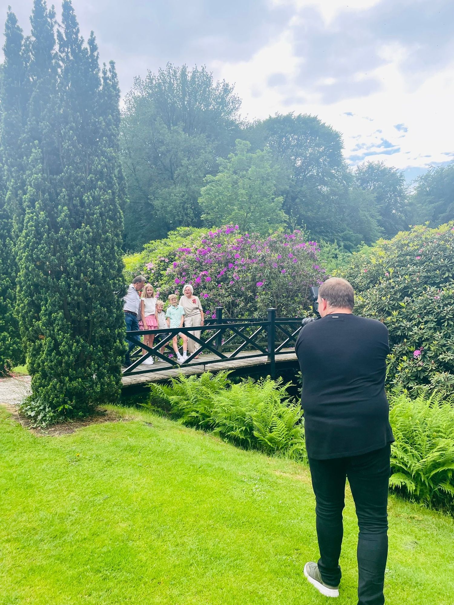 Fotograaf legt een gezin vast op een brug in een groene tuin met bloemen op de achtergrond.