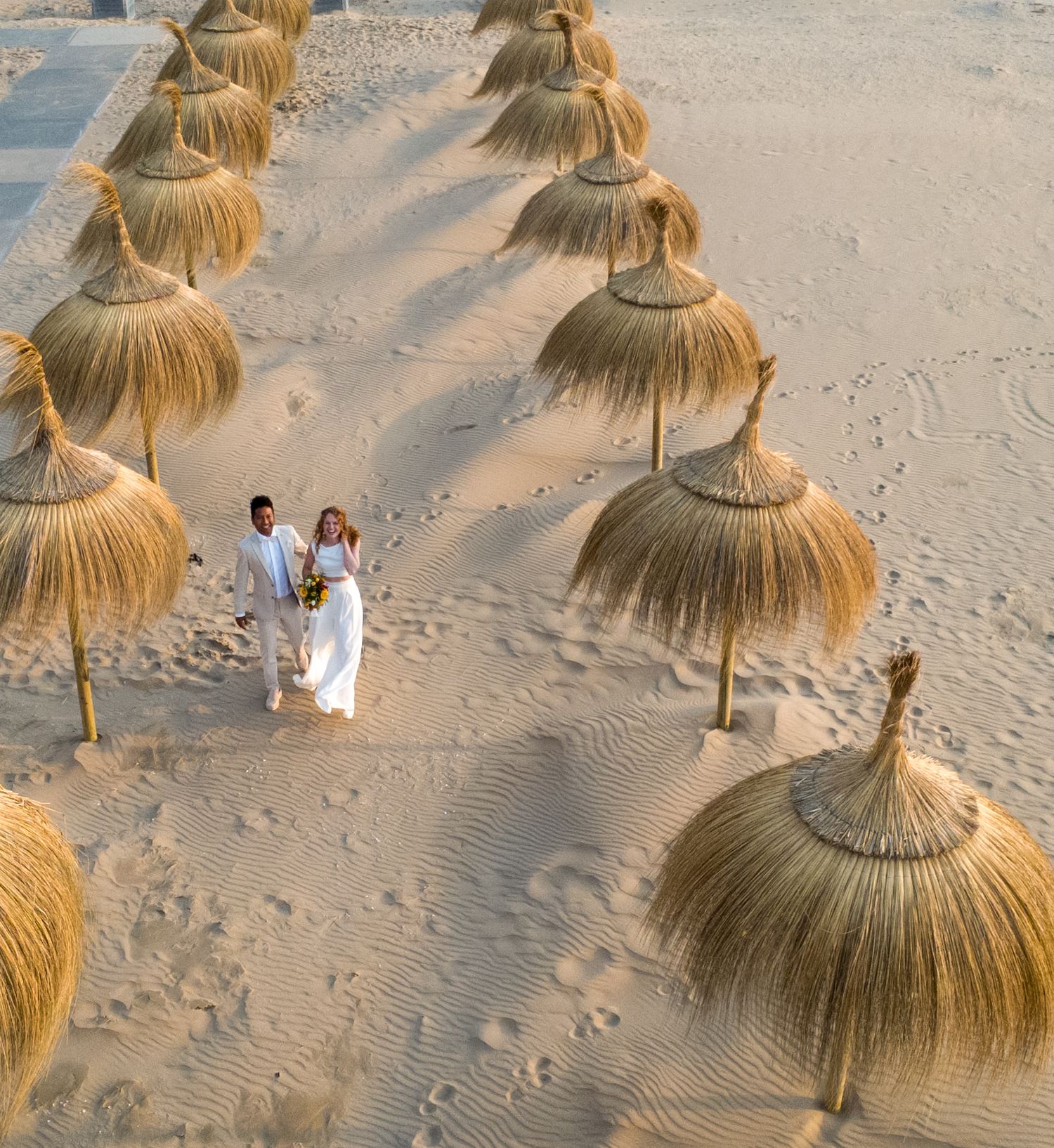 Drone foto van bruidspaar tussen rieten parasols, op het strand