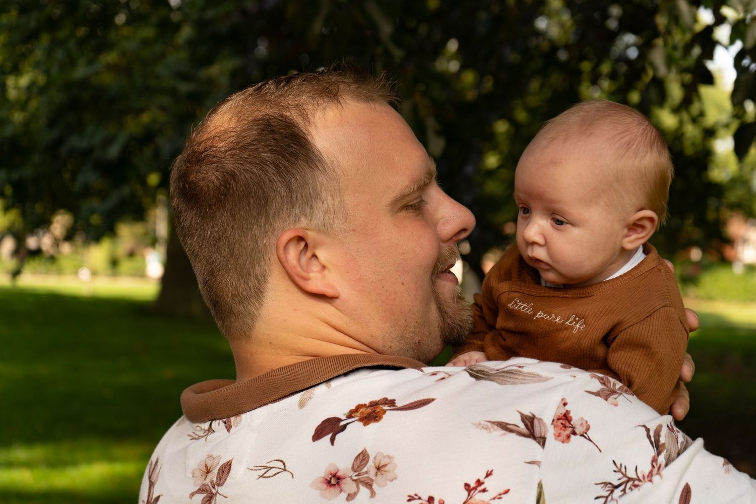 Vader kijkt lachend naar zijn baby, terwijl ze samen genieten van een moment buiten.