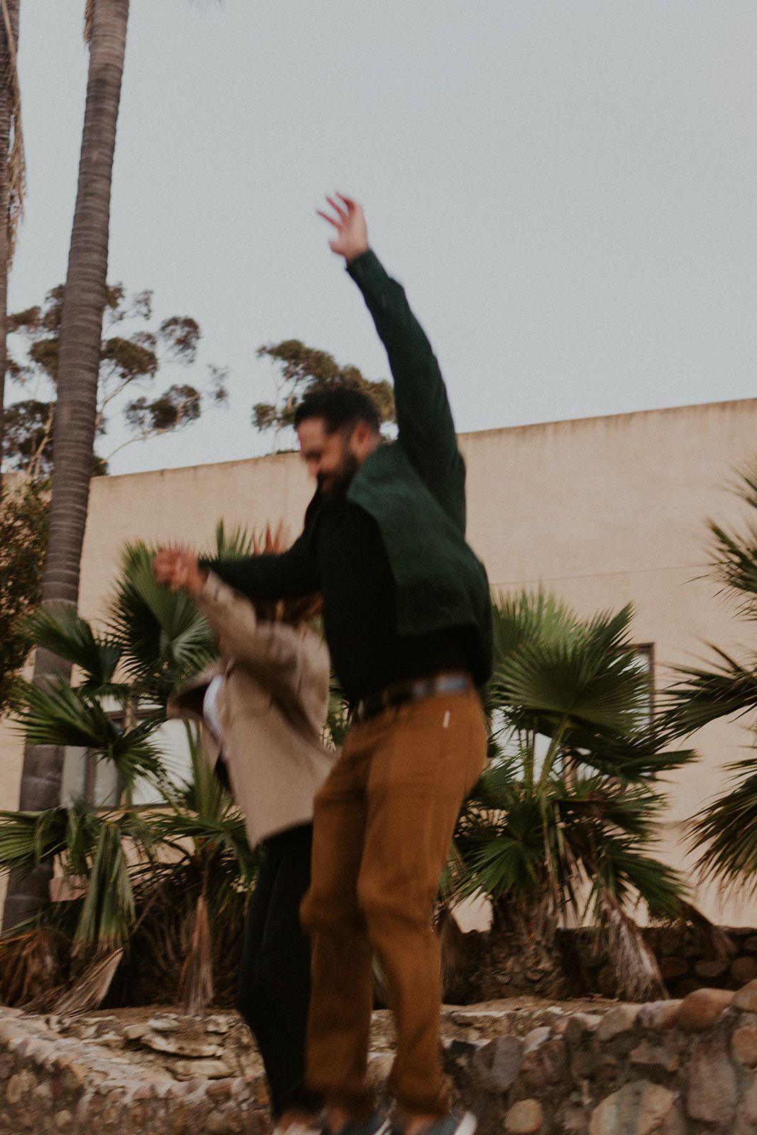 Candid desert session with playful movement, featuring palm trees and soft sunset tones in a warm, earthy landscape.