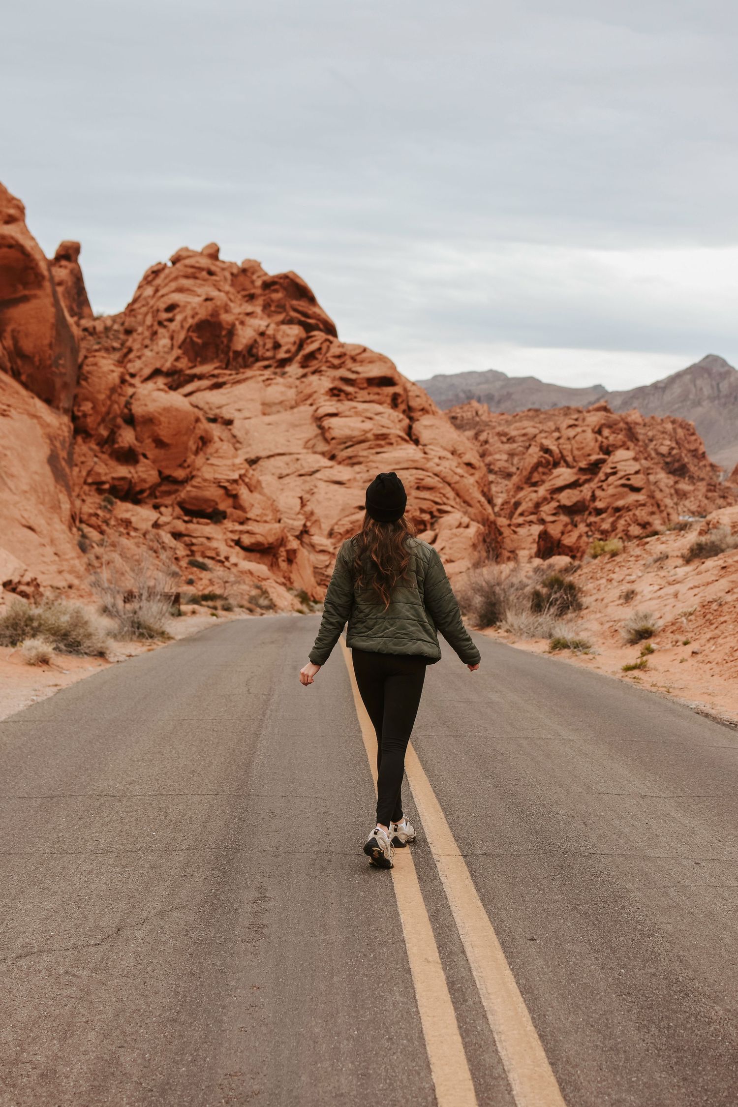 Solo destination session in the desert featuring a subject walking a scenic road surrounded by red canyon cliffs under open sky.