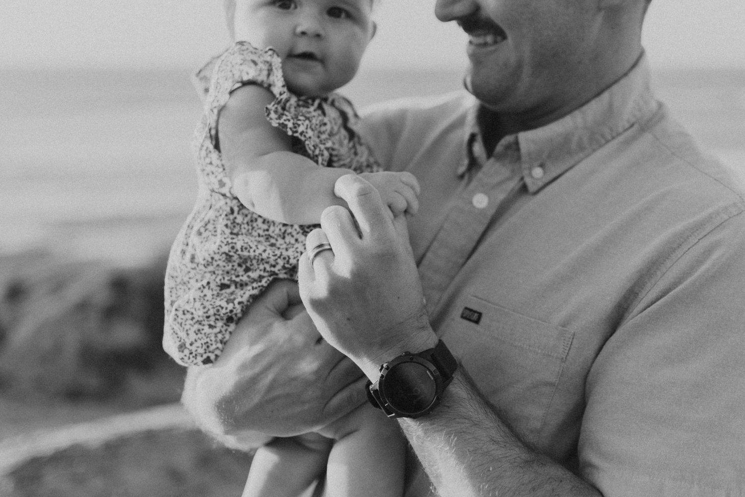 Black and white family portrait featuring a parent holding their baby during a candid outdoor session.