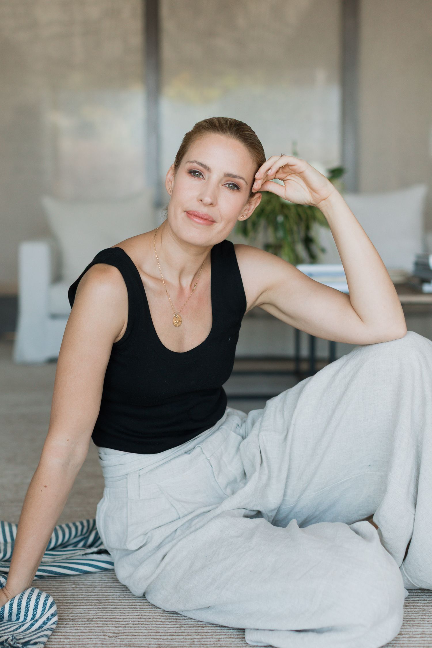 A person in a black sleeveless top relaxes on white bedding in a bright, modern interior setting.