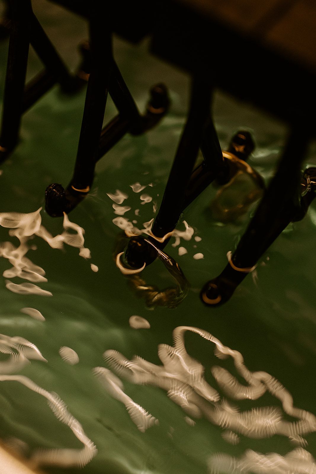 Close-up of black furniture legs with gold accents standing on a reflective green wet surface.