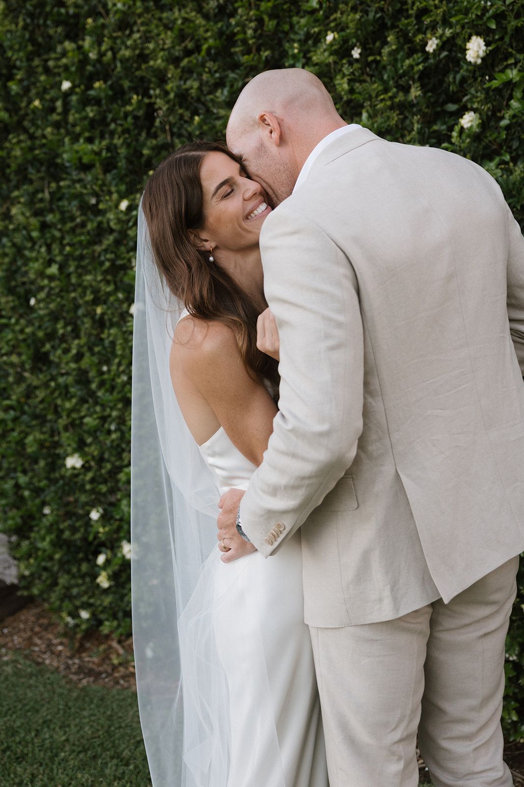 A romantic sequence of wedding photos showing a couple in white and beige attire embracing against a lush green hedge backdrop.