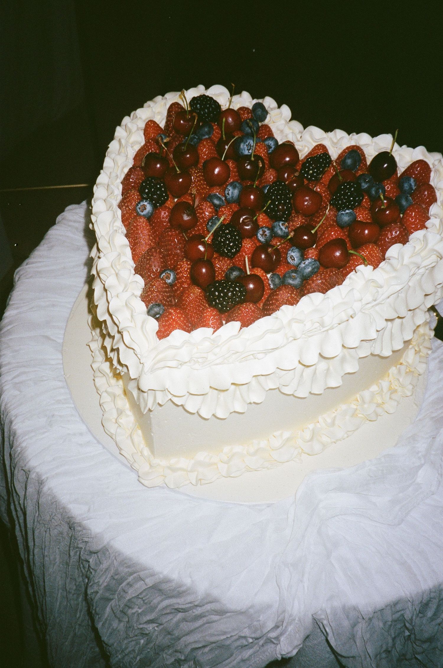 Heart-shaped white wedding cake decorated with fresh strawberries and blueberries on top.