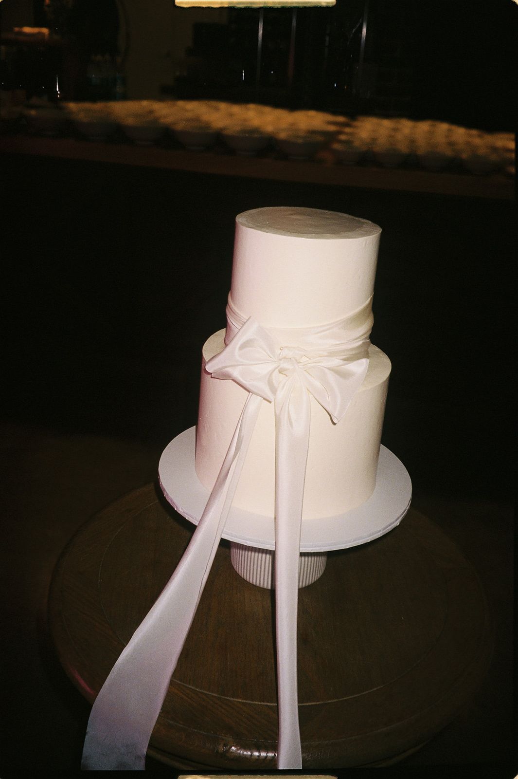Elegant two-tier white wedding cake with satin ribbon bow on white cake stand.