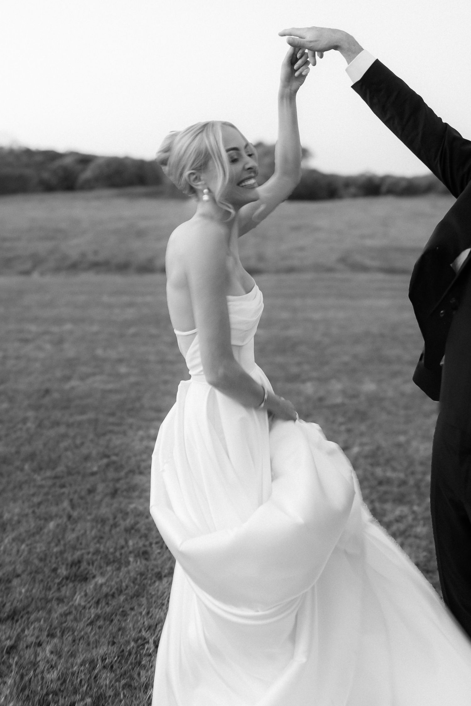 A couple shares a romantic dance together in an outdoor field, with the bride wearing a flowing white wedding gown.