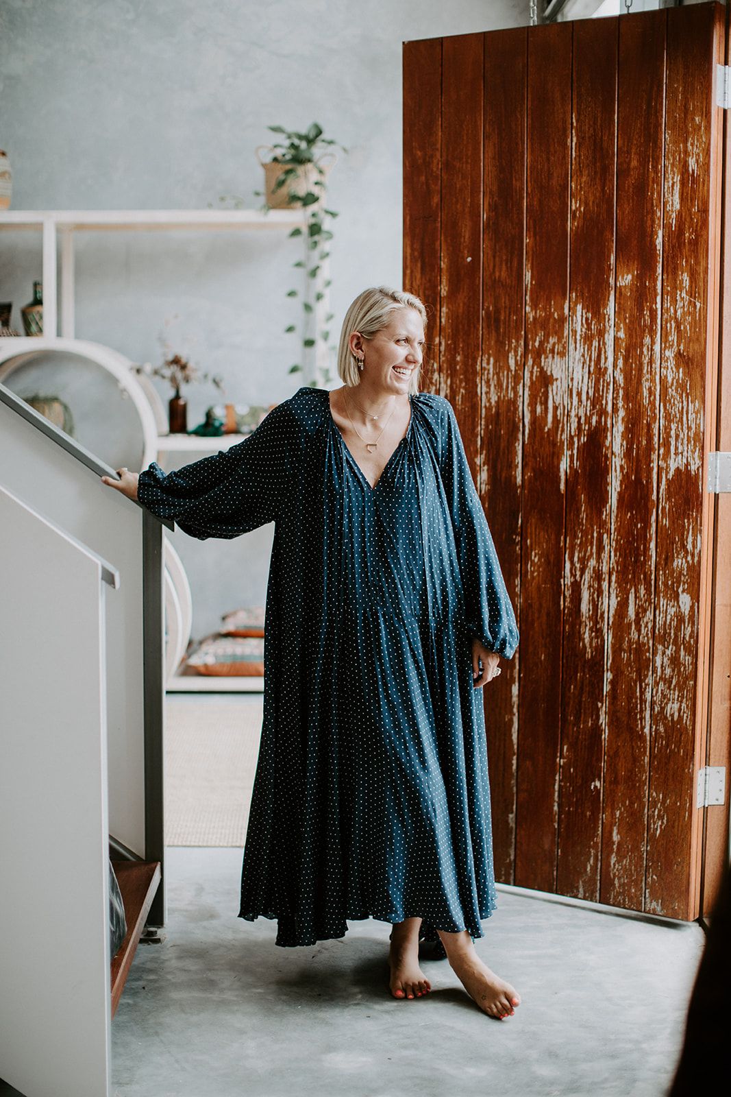 Navy blue linen dress hanging on wooden wall in minimalist interior setting with white walls and natural light.