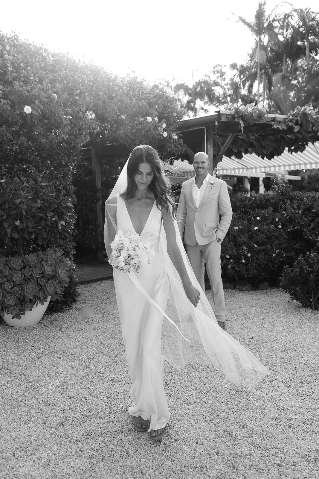 Black and white photo series showing a couple in wedding attire walking and dancing playfully in an outdoor garden setting.