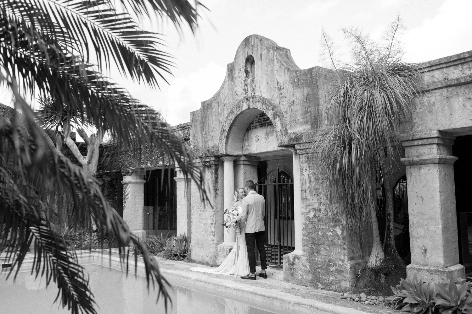 A historic Spanish colonial building entrance with palm fronds in the foreground, captured in black and white.